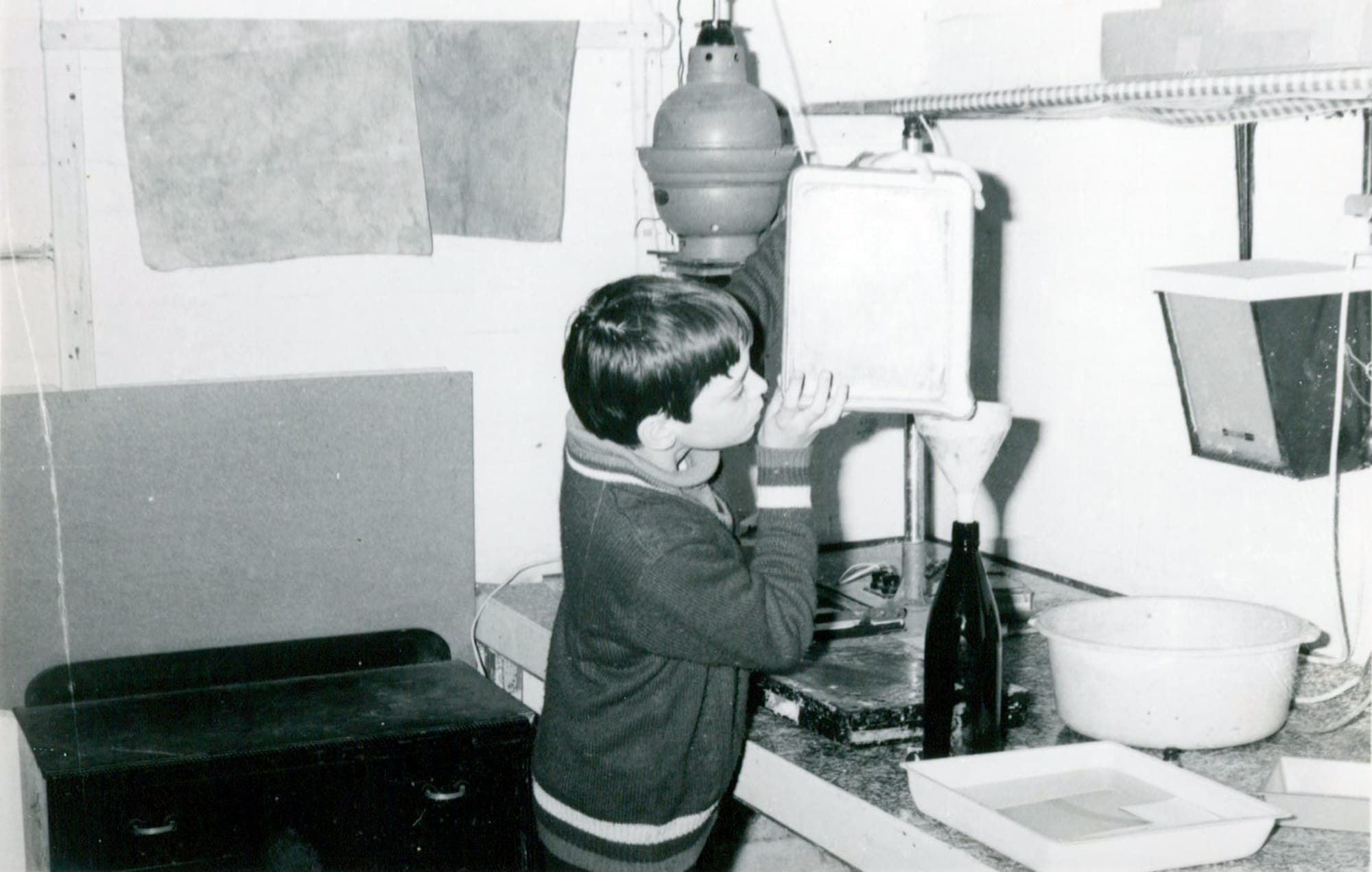 Thomas Judge aged about 13 working in a school darkroom, surrounded by an enlarger, developing trays and photographic equipment.